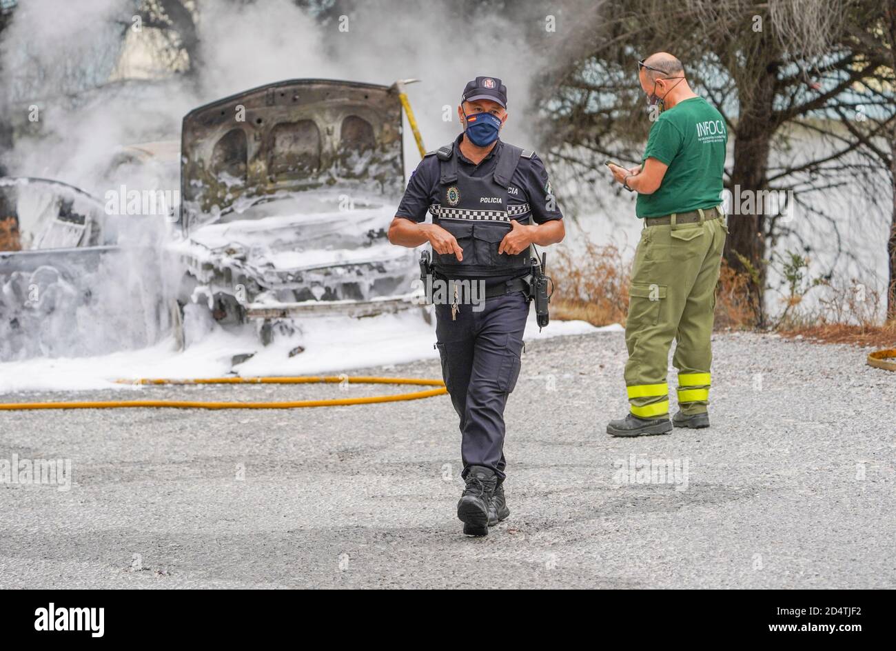 Feuerwehrleute löschen ein Feuer mit weißem Schaum auf einem brennenden Auto in einem Waldgebiet, Mijas, Spanien. Stockfoto