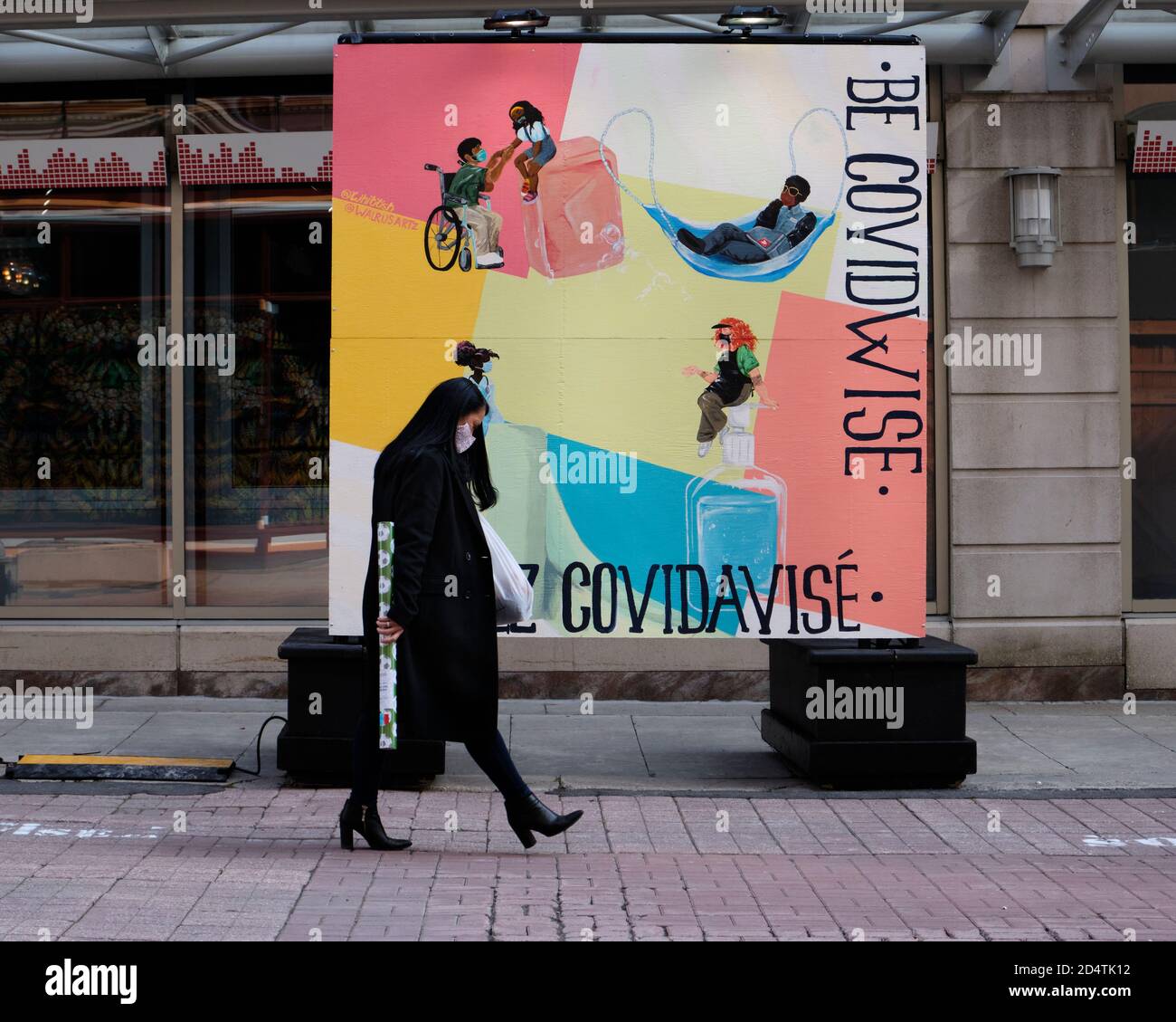 Ottawa, Kanada. Oktober 2020. Frau mit Maske, die an dem neuen 'Be CovidWise'-Poster auf der Sparks Street vorbei geht Stockfoto