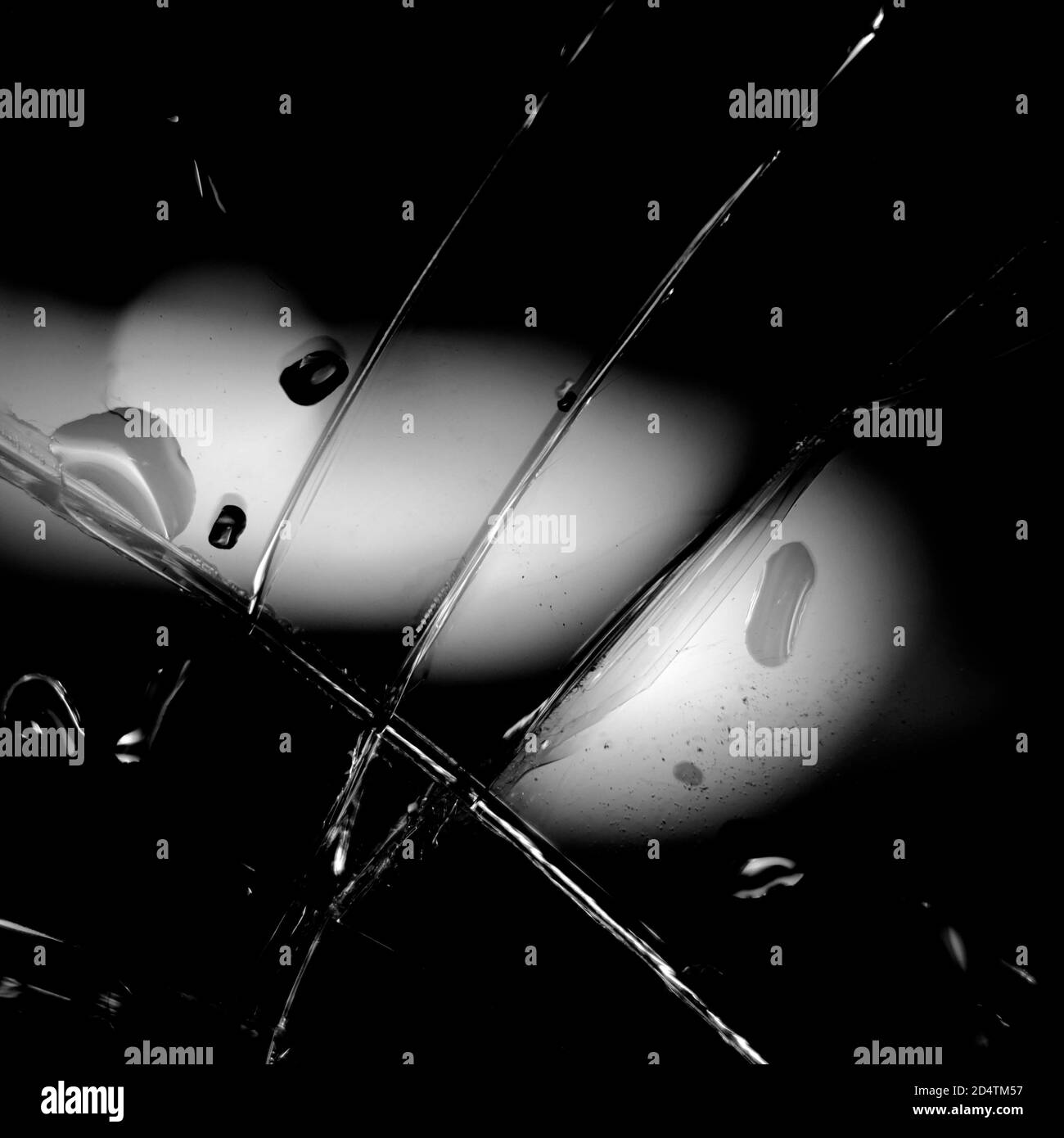 Gebrochener Glashintergrund in schwarz. Schwarzer minimalistischer Hintergrund mit Rissen auf dem Glas mit Wassertropfen. Stockfoto