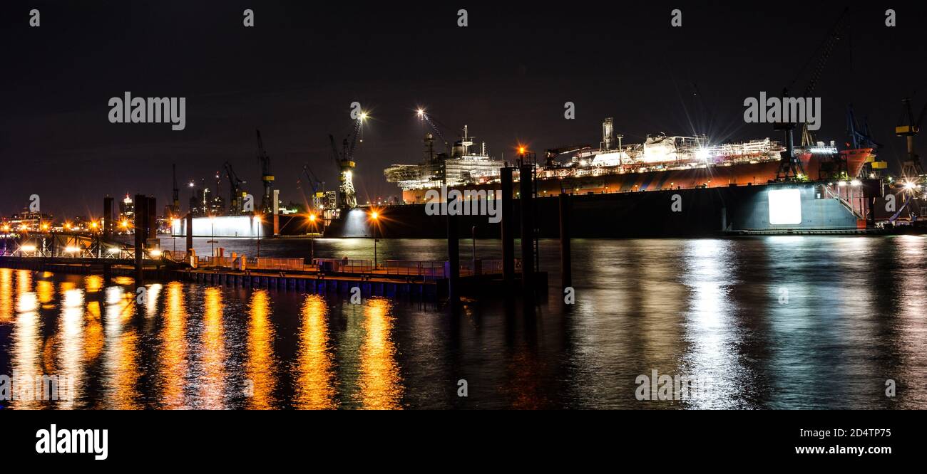 Szenische Breitbild-Nachtaufnahme eines großen Containerschiffes in Reparatur im Dock an der Elbe in Hamburg, Deutschland Stockfoto