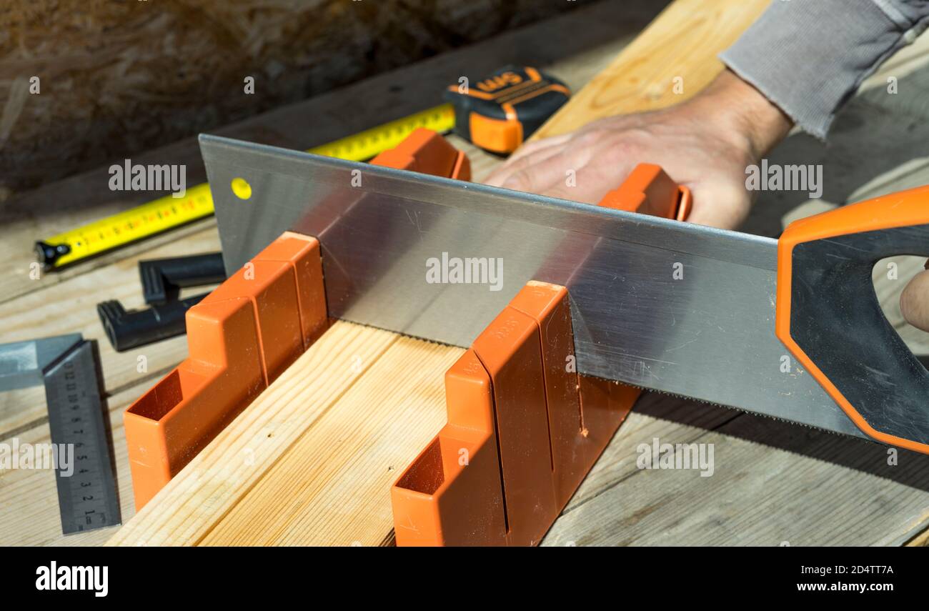 Mann schneidet eine Holzlatte mit einer Säge und Gehrungskasten. Nahaufnahme. Selektiver Fokus. Stockfoto