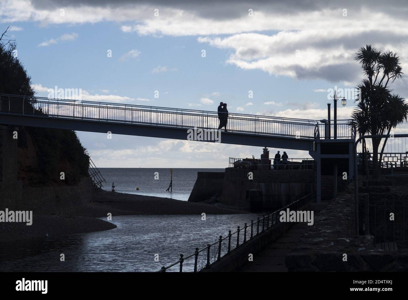 Sidmouth, Devon, 11. Okt 2020 Menschen überqueren die neu eröffnete Alma Bridge in Sidmouth, Teil des legendären South West Coastal Path. Die alte Brücke wurde geschlossen, da die Küstenerosion ihre Fundamente bedrohte, und die Arbeiten an der Ersetzung begannen im August 2019. Aufgrund der Coronavirus-Pandemie wurden die Arbeiten bis in diesem Frühjahr erheblich verzögert. Die neue Brücke überquert den Fluss Sid, und Bewohner und Wanderer können den südwestlichen Küstenweg ohne Umleitung ins Landesinnere fortsetzen. Kredit: Photo Central/Alamy Live Nachrichten Stockfoto