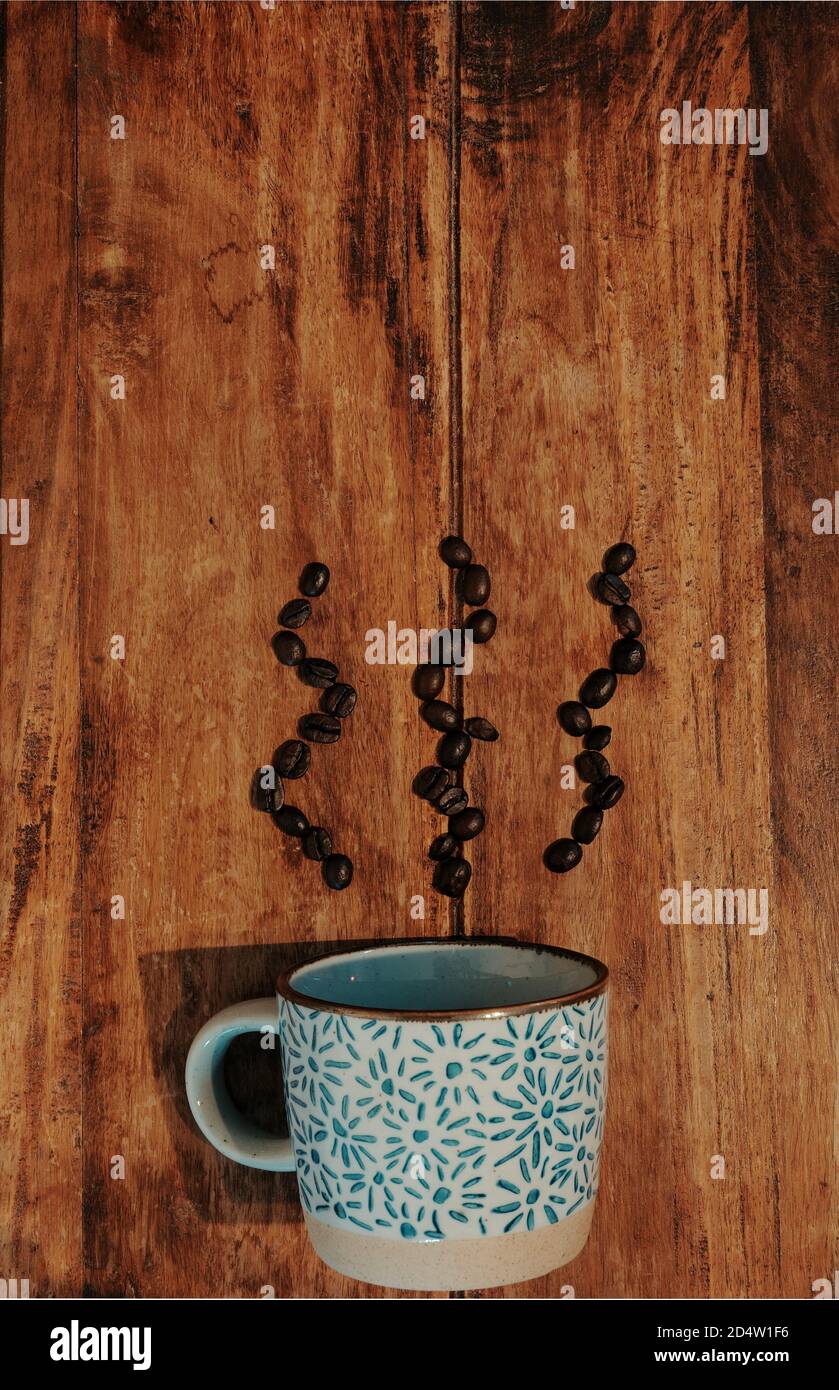 Kaffeetasse auf Holztisch, Kaffeebohnen auf Tisch in Dampfmuster. Draufsicht, vertikale Komposition. Stockfoto