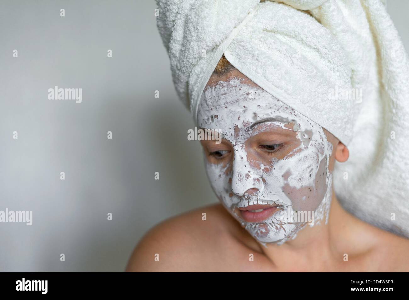 Schüchterne Frau auf einem weißen Hintergrund saubere Gesichtscreme auf Gesicht Handtuch im Haar auf dem Kopf. Stockfoto