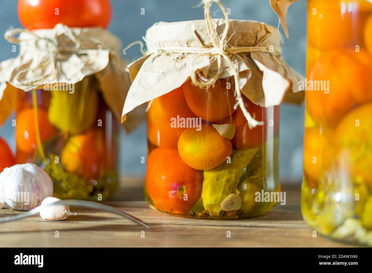 Hausgemachte Gläser mit eingelegten Tomaten und Gurken auf rustikalem Holzhintergrund. Eingelegtes und konservierte Produkt. Fermentierte Tomaten auf dunklem Hintergrund. Stockfoto