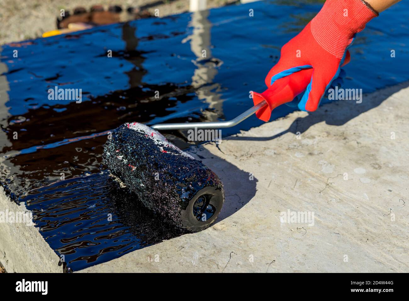 Imprägnierbeschichtung. Arbeiter Hand in Schutzhandschuhe trägt Bitumenmastix auf dem Fundament. Dachdecker decken die Dach Polymer modifizierten Bitumen Imprägnierung Primer, mit einer Walzenbürste. Selektiver Fokus. Leerzeichen für Text. Stockfoto