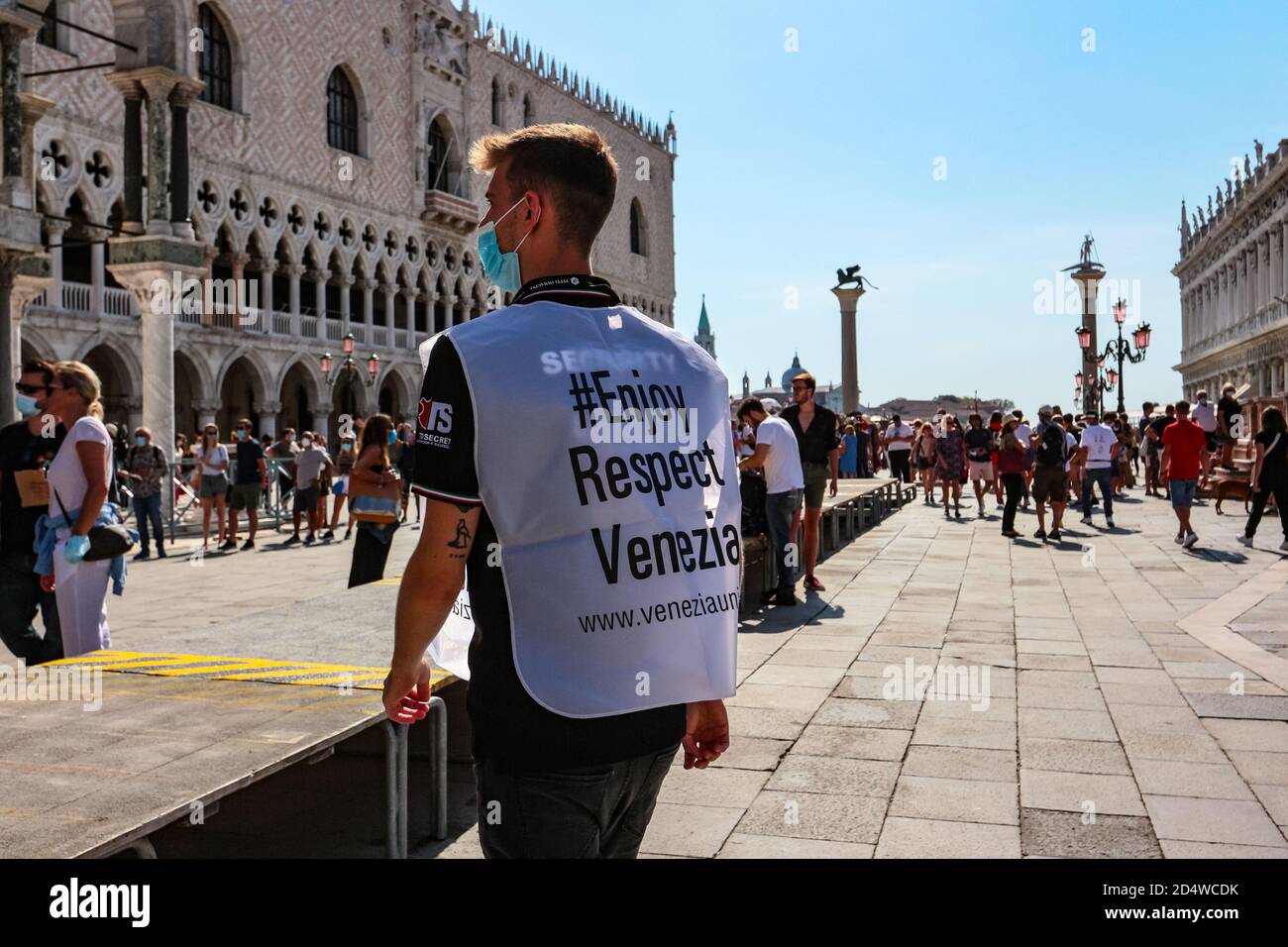 '#enjoy respect Venezia' Wache in chirurgischer Gesichtsmaske repräsentiert verantwortungsvollen Tourismus auf dem Markusplatz während der Coronavirus-Krise. Stockfoto