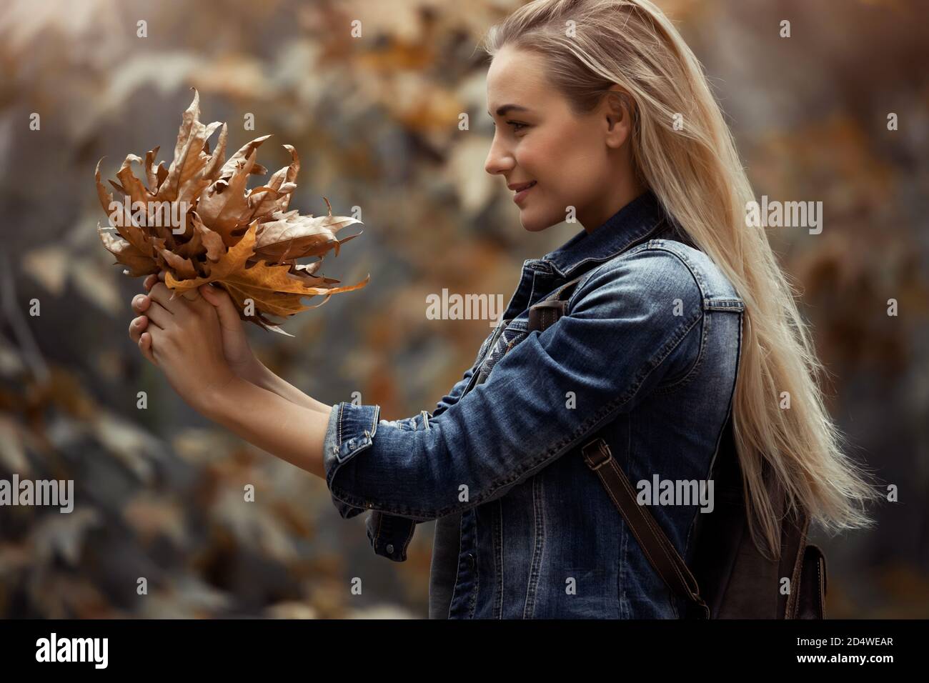 Profil Portrait eines schönen blonden Mädchens mit schönem Blumenstrauß von trockenen Baumblättern im Park. Genießen Sie die Schönheit der Natur im Herbst. Stockfoto