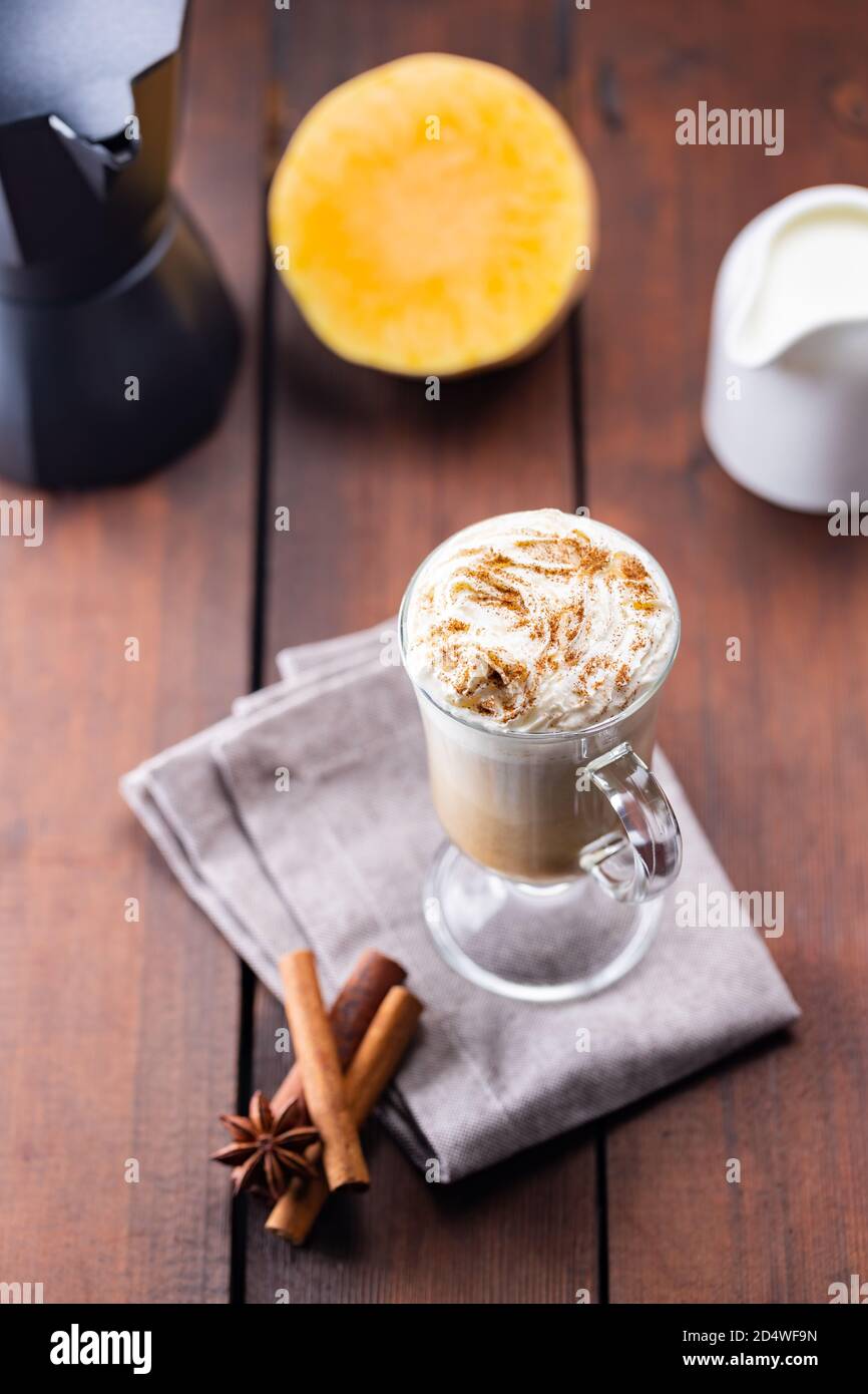 Kürbislatte, Milchkännchen und ein Stück Kürbis. Kürbislatte mit Schlagsahne und Gewürzen auf Holzbrettern. Heißer Herbstkaffee auf einem Laken-Nickerchen Stockfoto
