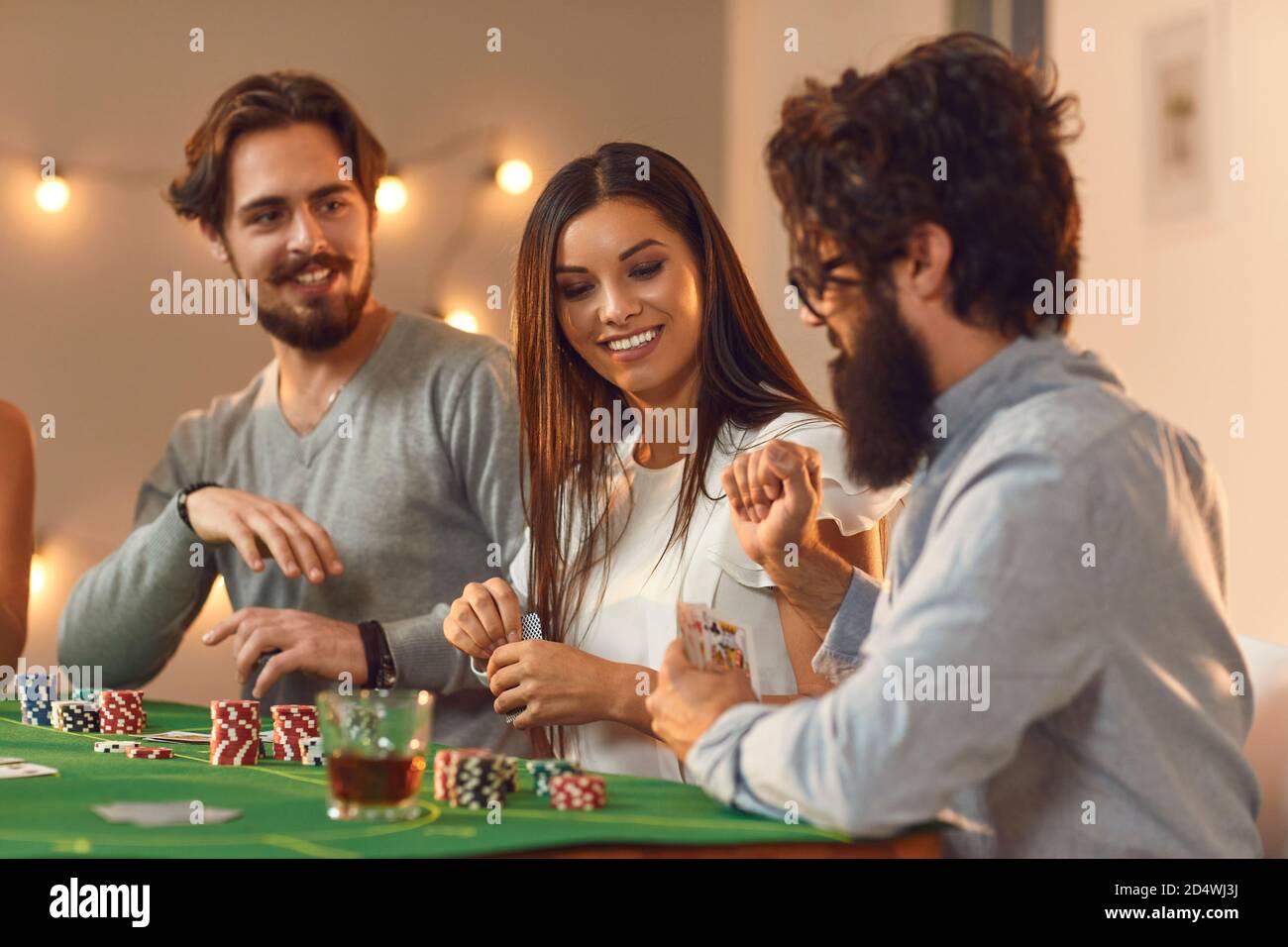 Glückliche junge Leute spielen Poker sitzen am Tisch mit Getränken Bei Casino-Motto-Party Stockfoto