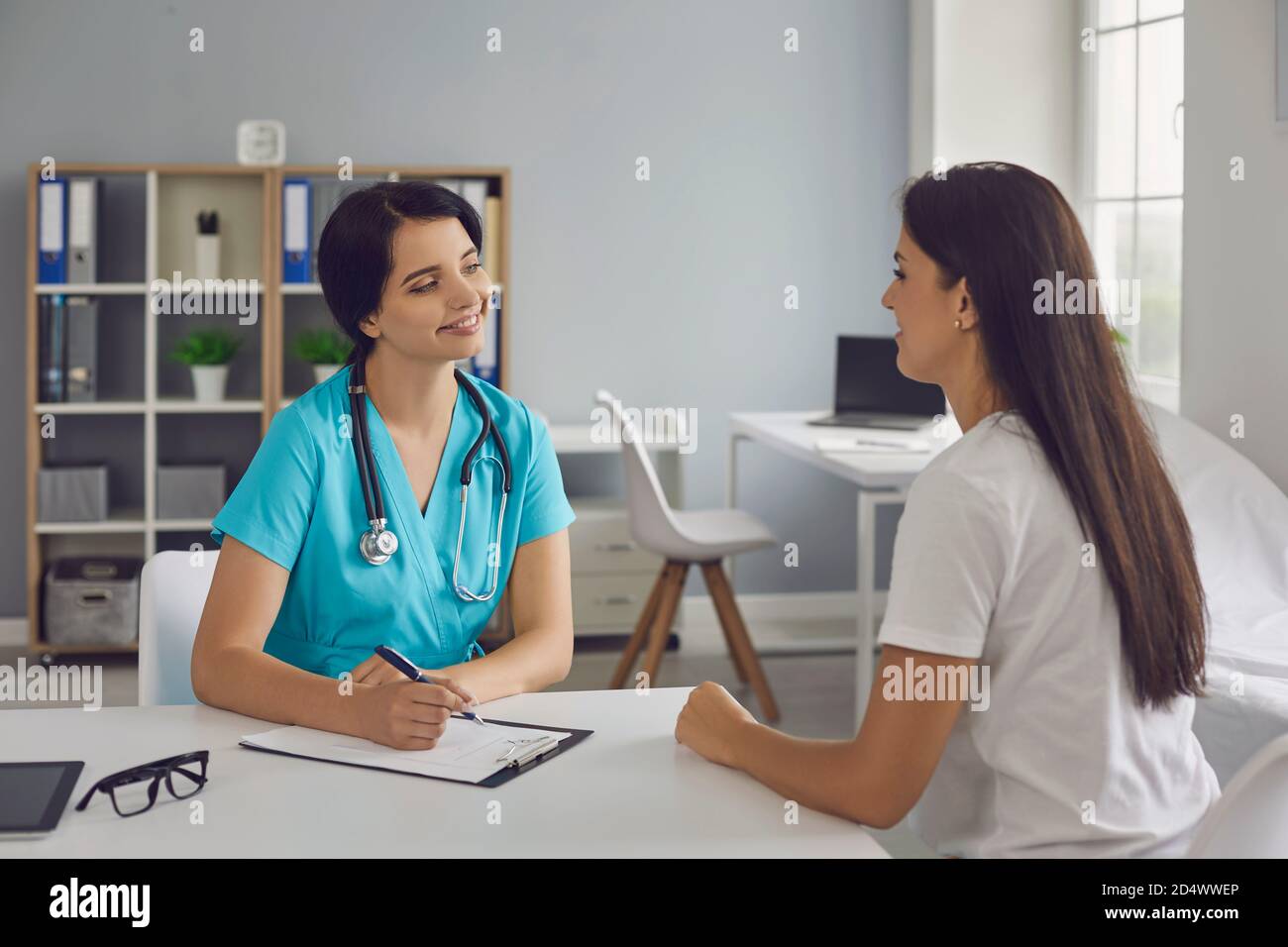 Junge lächelnde Arzt hören Frau Patienten Beschwerden in medizinischen Klinik Stockfoto