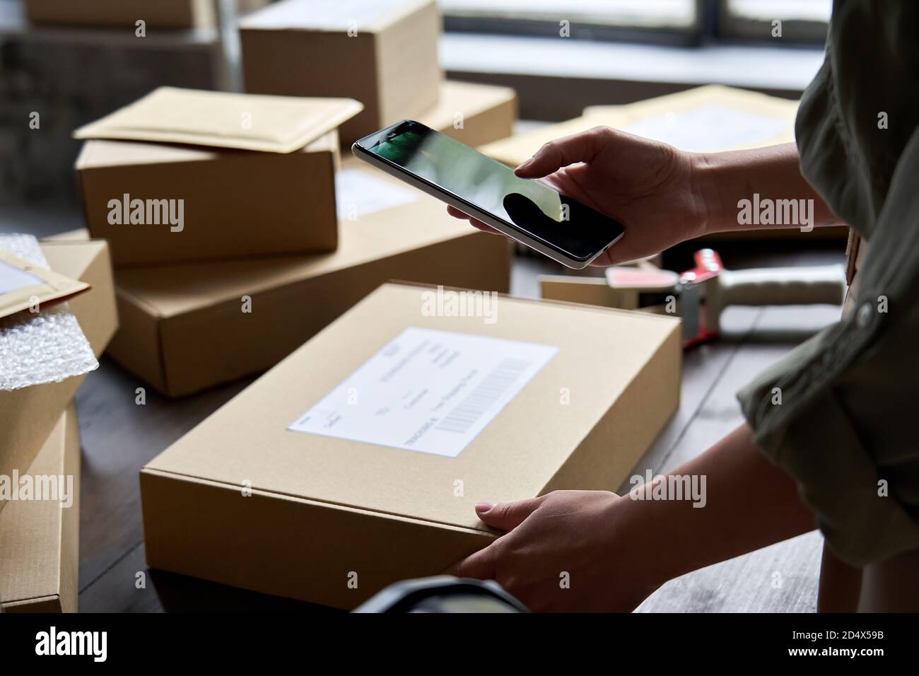 Weibliche Lagerarbeiterin, die den Paketkasten über eine mobile Anwendung hält. Stockfoto