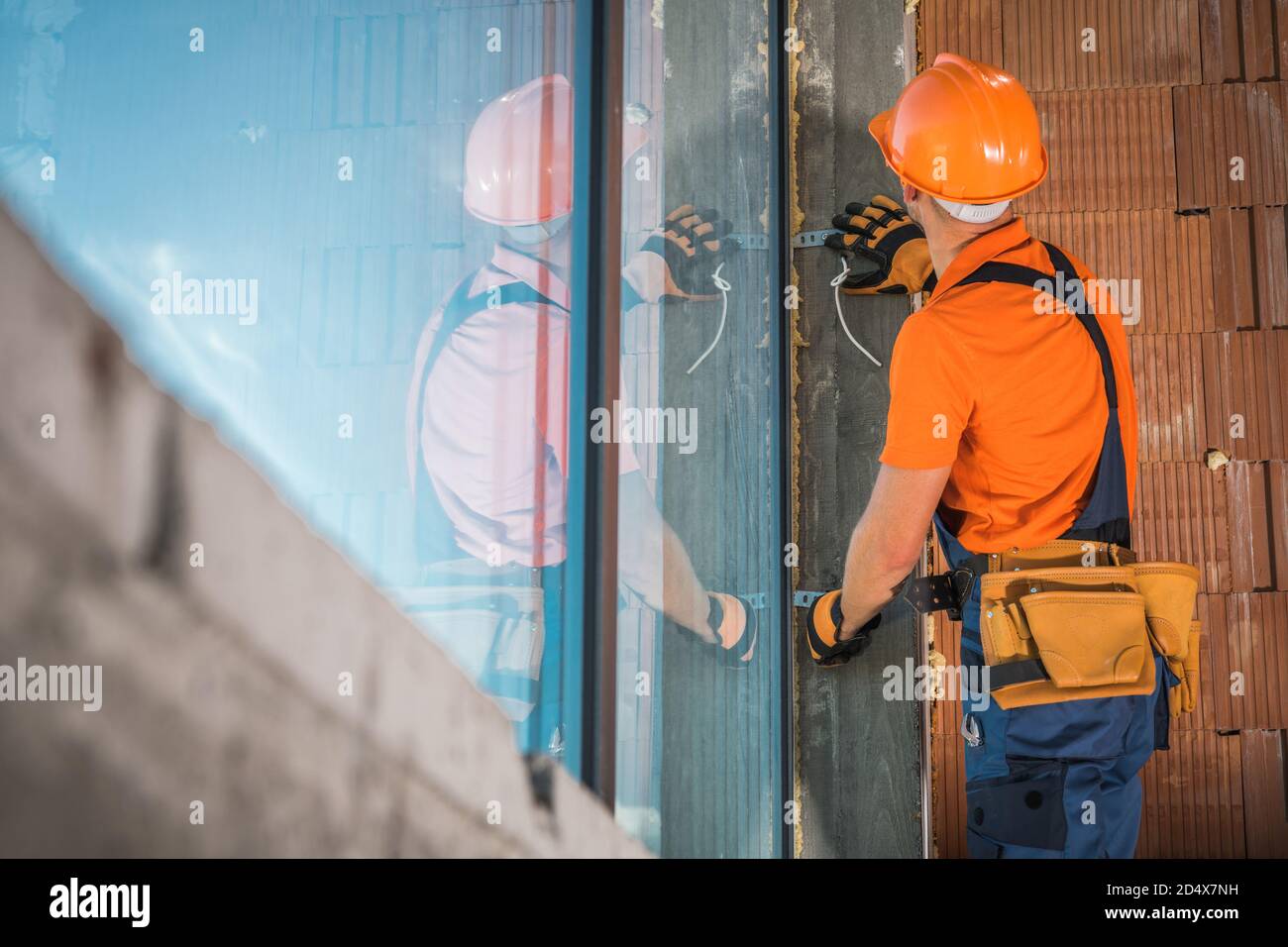 Kommerzielle Gebäude Windows Installation von kaukasischen Auftragnehmer Arbeiter in seinen 40er Jahren trägt Orange Tshirt und Hard hat. Industriedesign. Stockfoto