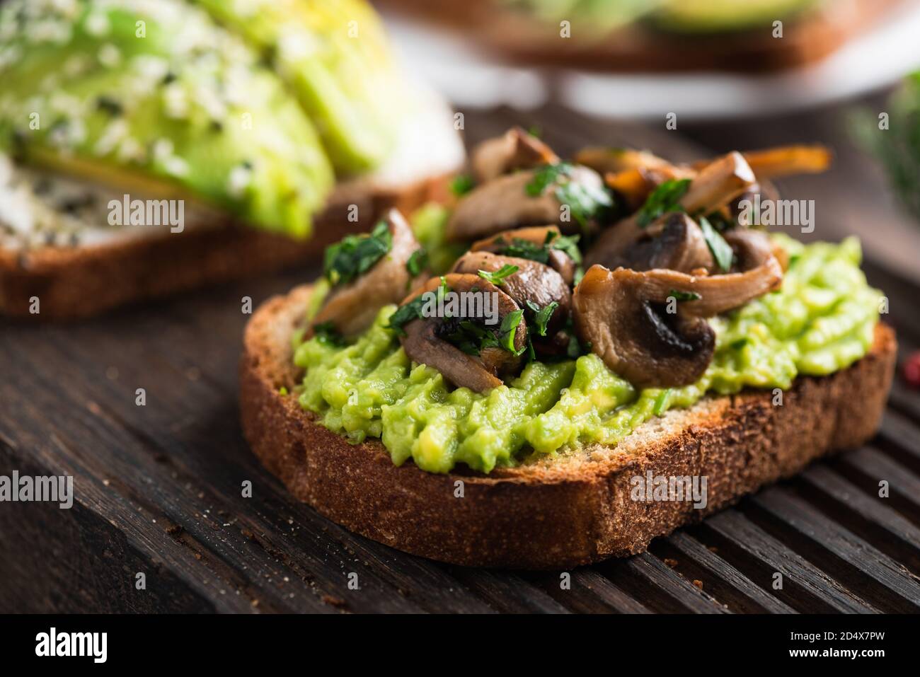 Avocado Toast mit gebratenen Pilzen garniert mit gehackter Petersilie. Gesunde vegane Avocado Toast Stockfoto