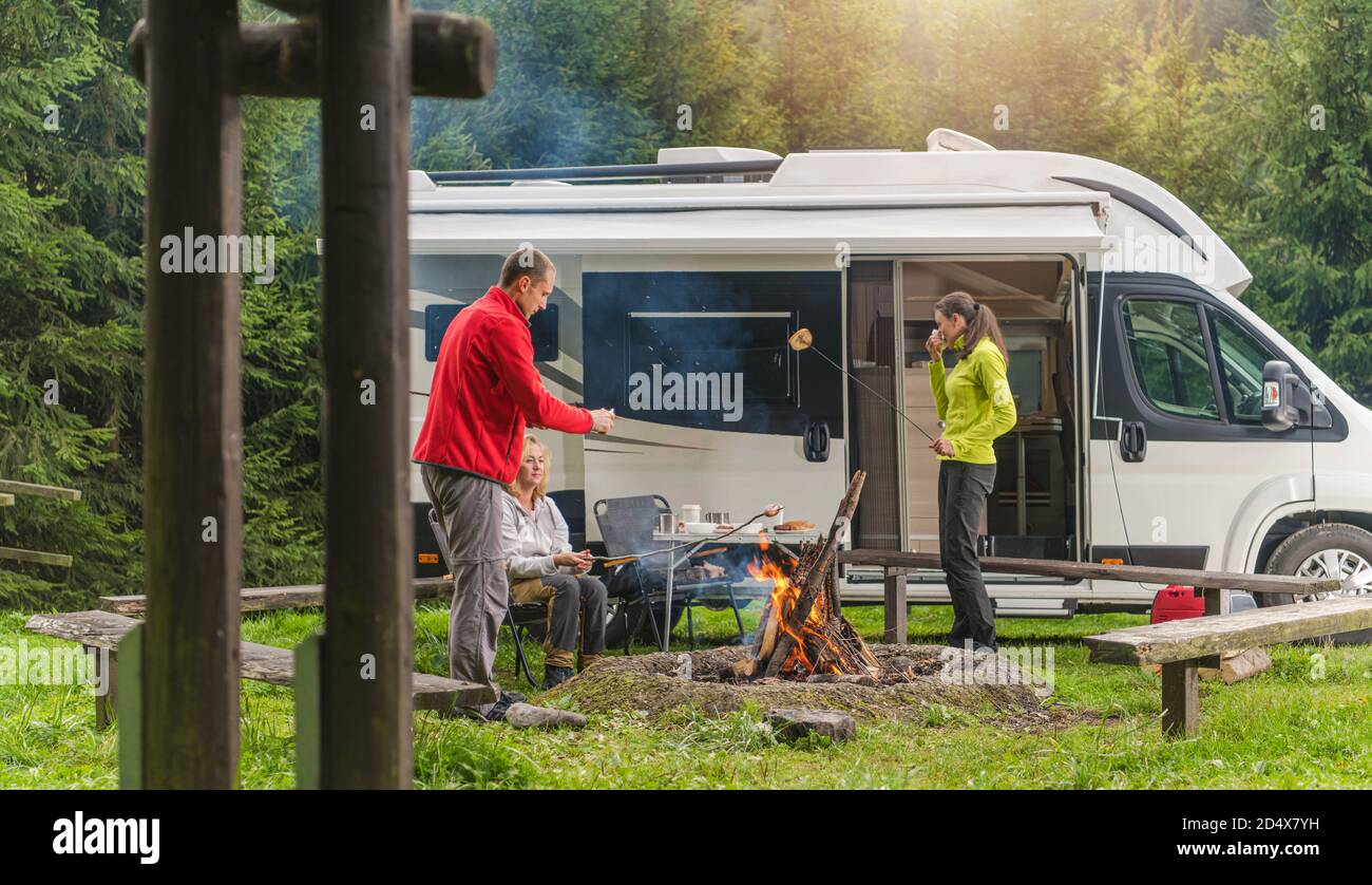 Drei kaukasische Freunde in ihren späten 30er Jahren, ein Mann und zwei Frau mit Spaß auf Wildnis Camping mit modernen Wohnmobil Camper Van. Gegrilltes Brot und Polnisch Stockfoto