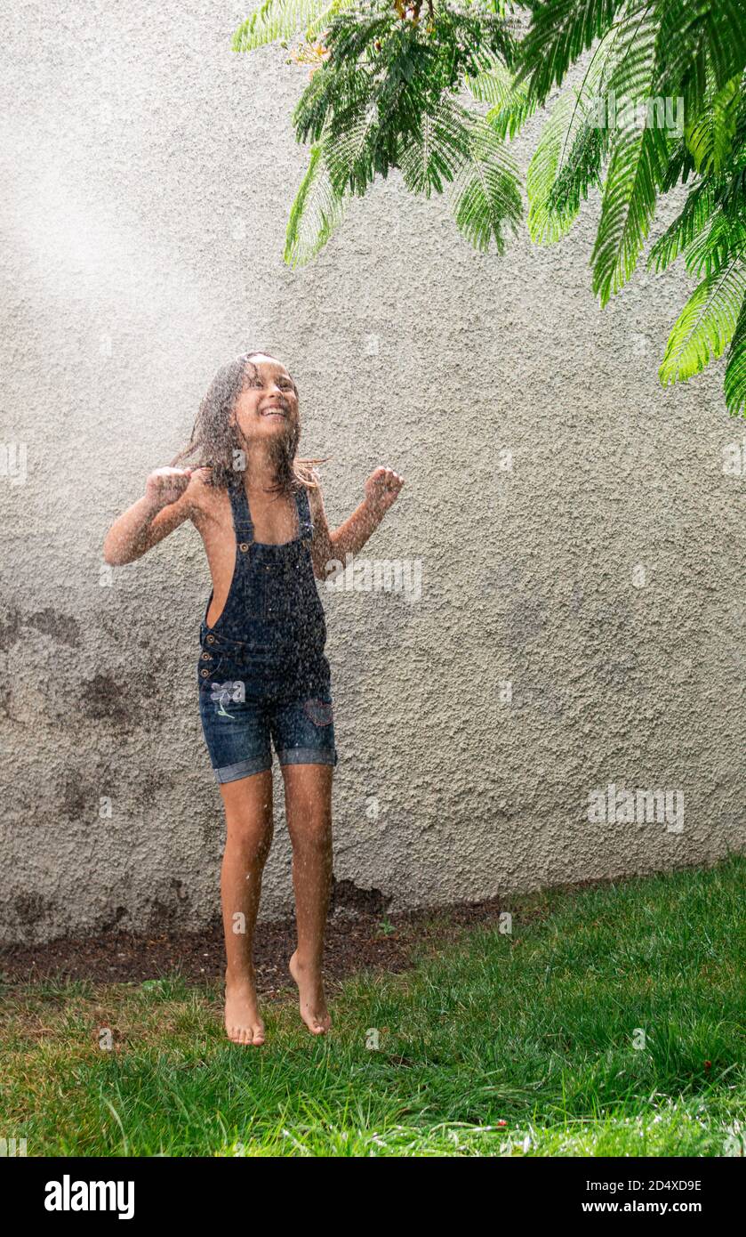 Ein entzückendes glückliches kleines Mädchen springen und Spaß in Ein Garten unter einem plätschernden Wasser Stockfoto