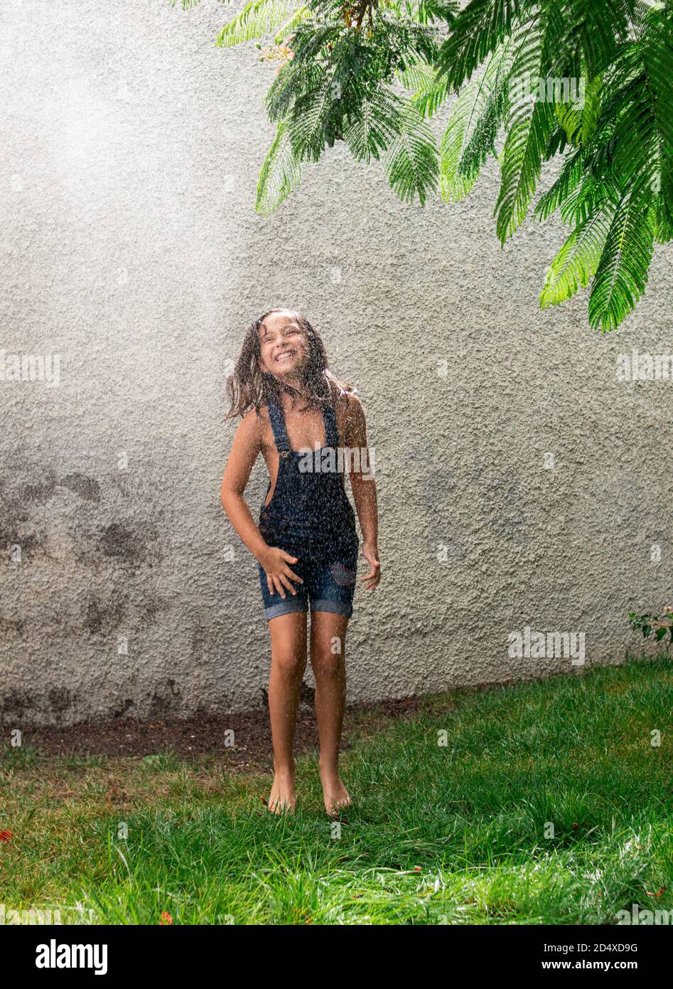Ein entzückendes glückliches kleines Mädchen springen und Spaß in Ein Garten unter einem Sprühwasser Stockfoto