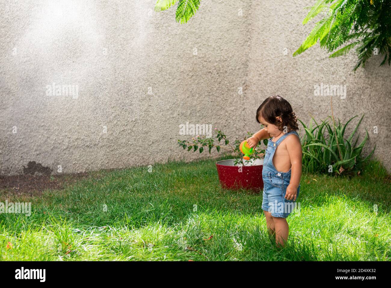 Eye-Level-Aufnahme eines niedlichen Mädchen mit einem Gießkanne Kann unter Spritzwasser in einem Garten spielen Stockfoto