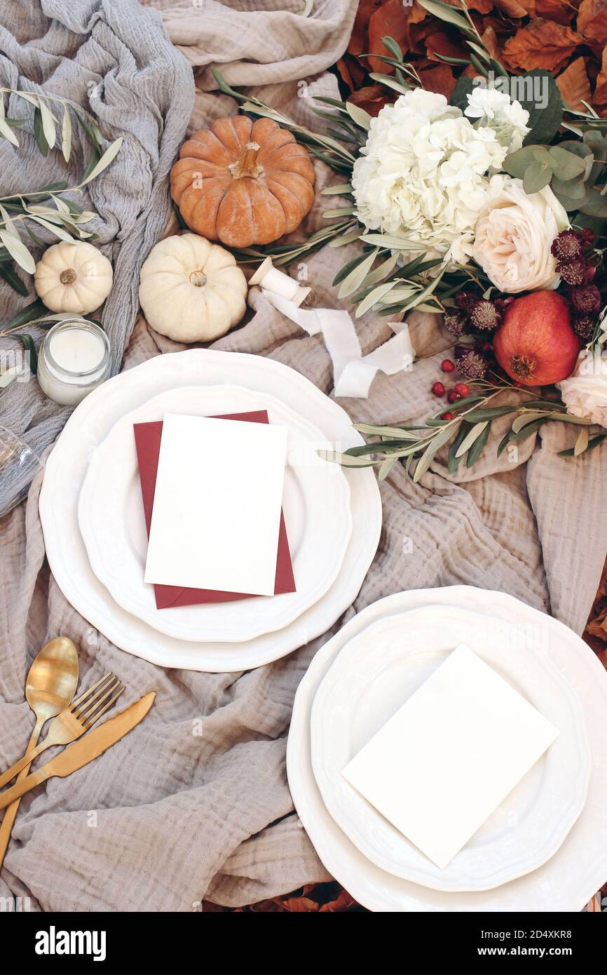Herbsttisch mit goldenem Besteck, Olivenzweigen und Porzellantellern. Kürbisse und Granatapfelfrüchte. Leere Karten Mockups. Herbst, Erntedankfest Stockfoto