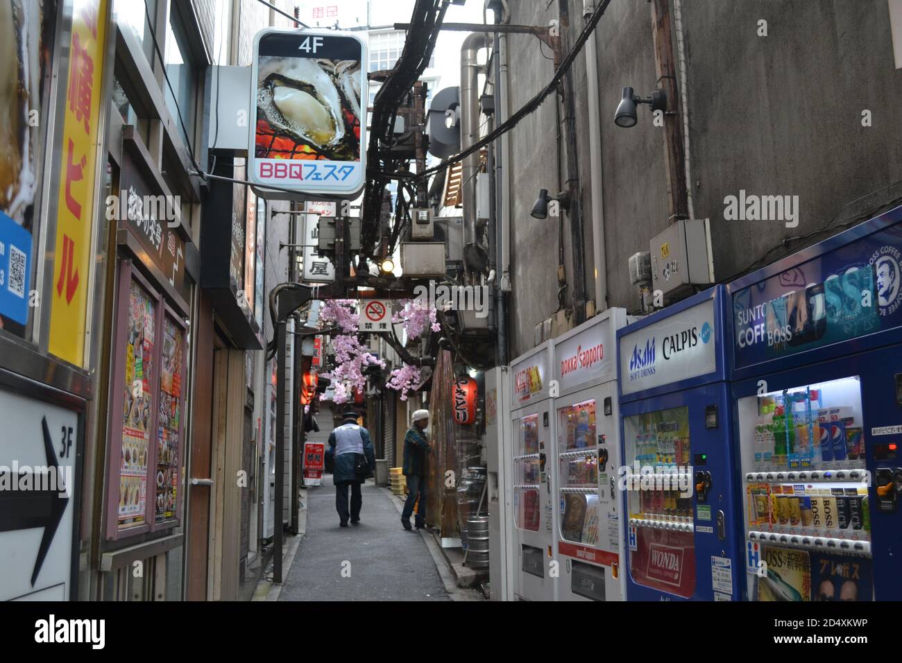 Tokio, Japan-2/24/16: In einer Gasse in Shinjuku macht sich ein Patrouillenmann auf den Weg. An den Seiten sehen wir verschiedene japanische Automaten. Stockfoto