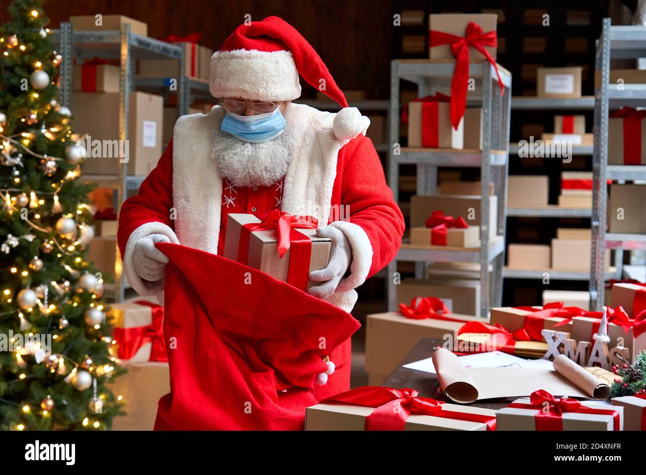 Santa trägt Kostüm Gesichtsmaske Verpackung Geschenke in der Tasche. Sichere Lieferung zu Weihnachten. Stockfoto