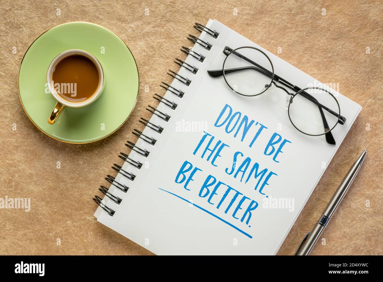 Seien Sie nicht gleich, seien Sie besser. Inspirierendes Schreiben in einem Spiral-Notizbuch mit einer Tasse Kaffee. Selbstverbesserung und persönliches Entwicklungskonzept. Stockfoto