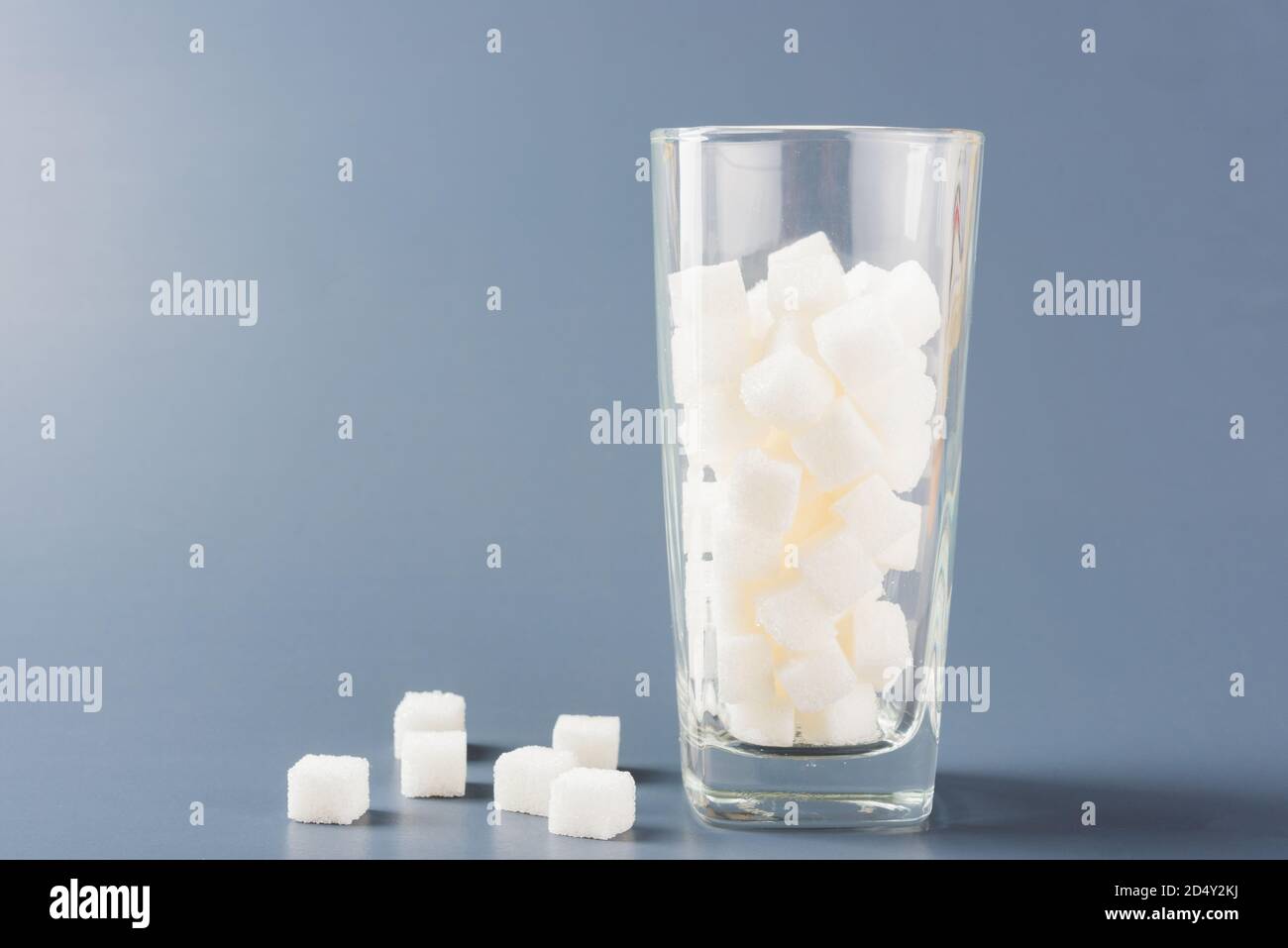 Ein Glas voller weißer Zuckerwürfel süße Lebensmittel Zutat, Studio Schuss auf einem grauen Hintergrund isoliert, Gesundheit hohes Blutrisiko von Diabetes und Kalorien inta Stockfoto