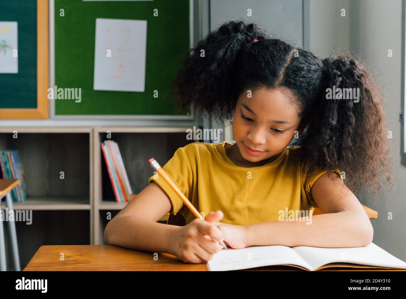 Afroamerikanische Schulmädchen sitzen in der Schule schriftlich in Notiz Buch mit Bleistift, Studium, Bildung, Lernen. Studentin am Schreibtisch im Klassenzimmer in der Prüfung. Stockfoto
