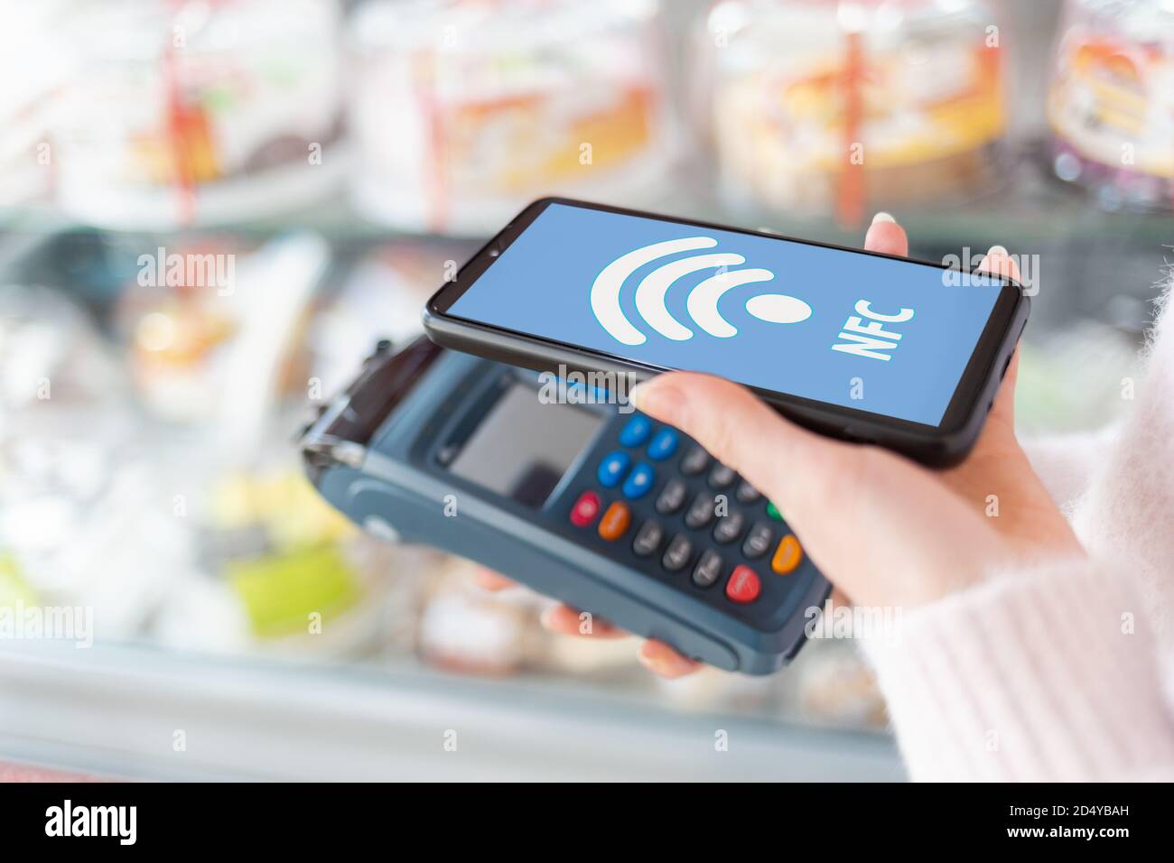 Die Hände einer Frau in der Nähe hält ein Zahlungsterminal und bezahlt für einen Kauf mit einem Smartphone. Auf dem Telefonbildschirm das wi-Fi-Netzwerk. Die Conce Stockfoto