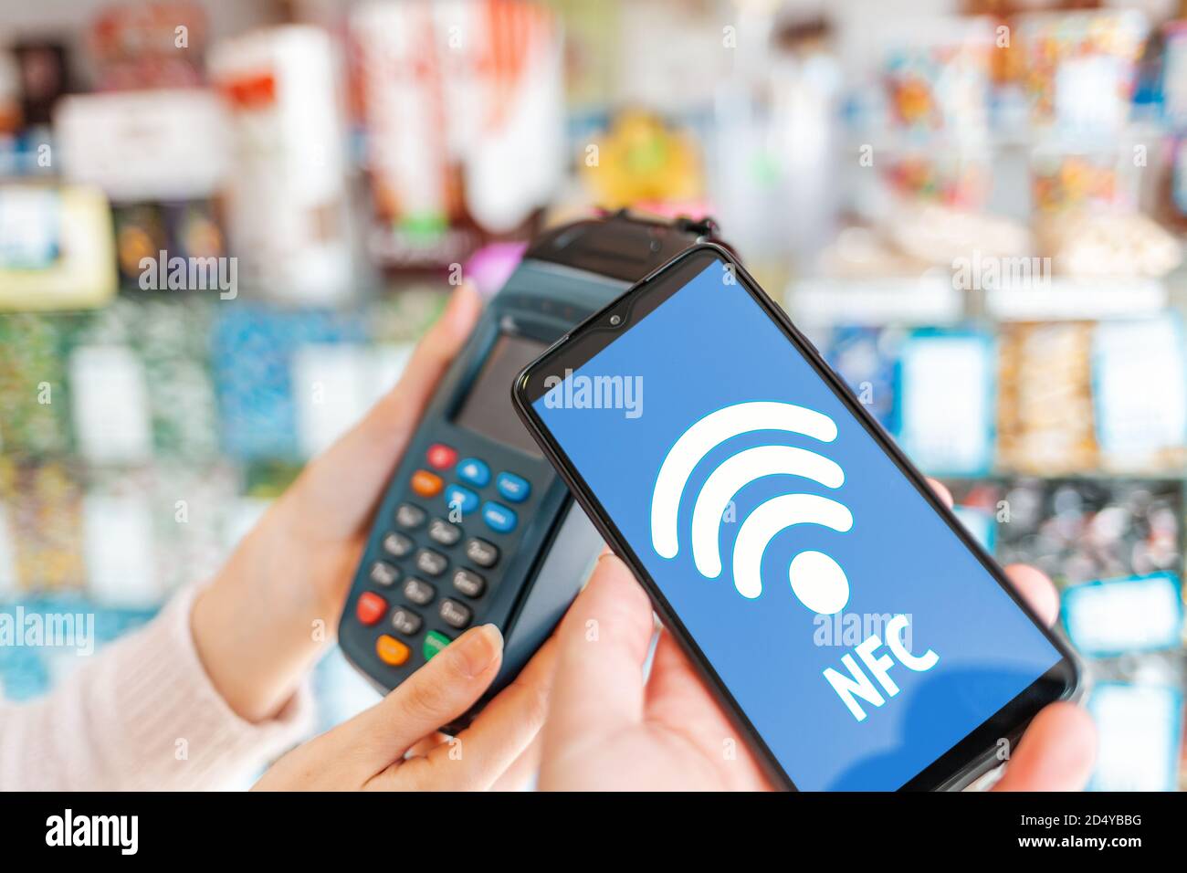 Die Hände der Frauen werden von einem Zahlungsterminal gehalten und ein Mann bezahlt für einen Kauf mit einem Smartphone.auf dem Bildschirm des Telefons, das wi-Fi-Netzwerk. Nahaufnahme. Die CO Stockfoto