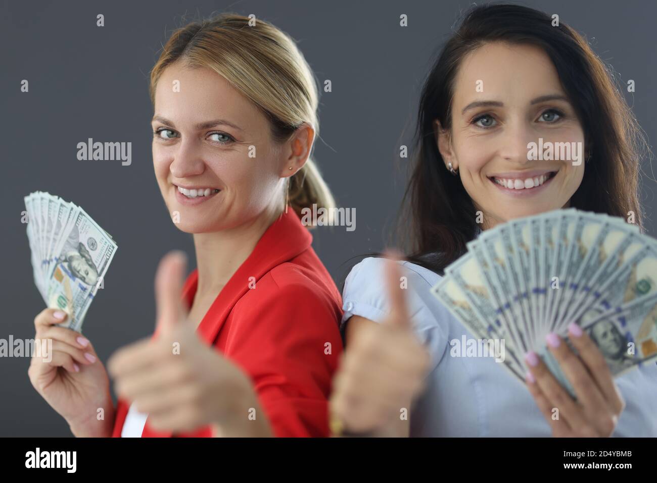 Zwei Frauen stehen mit Geldbündel und zeigen Daumen Geste im Hochformat Stockfoto