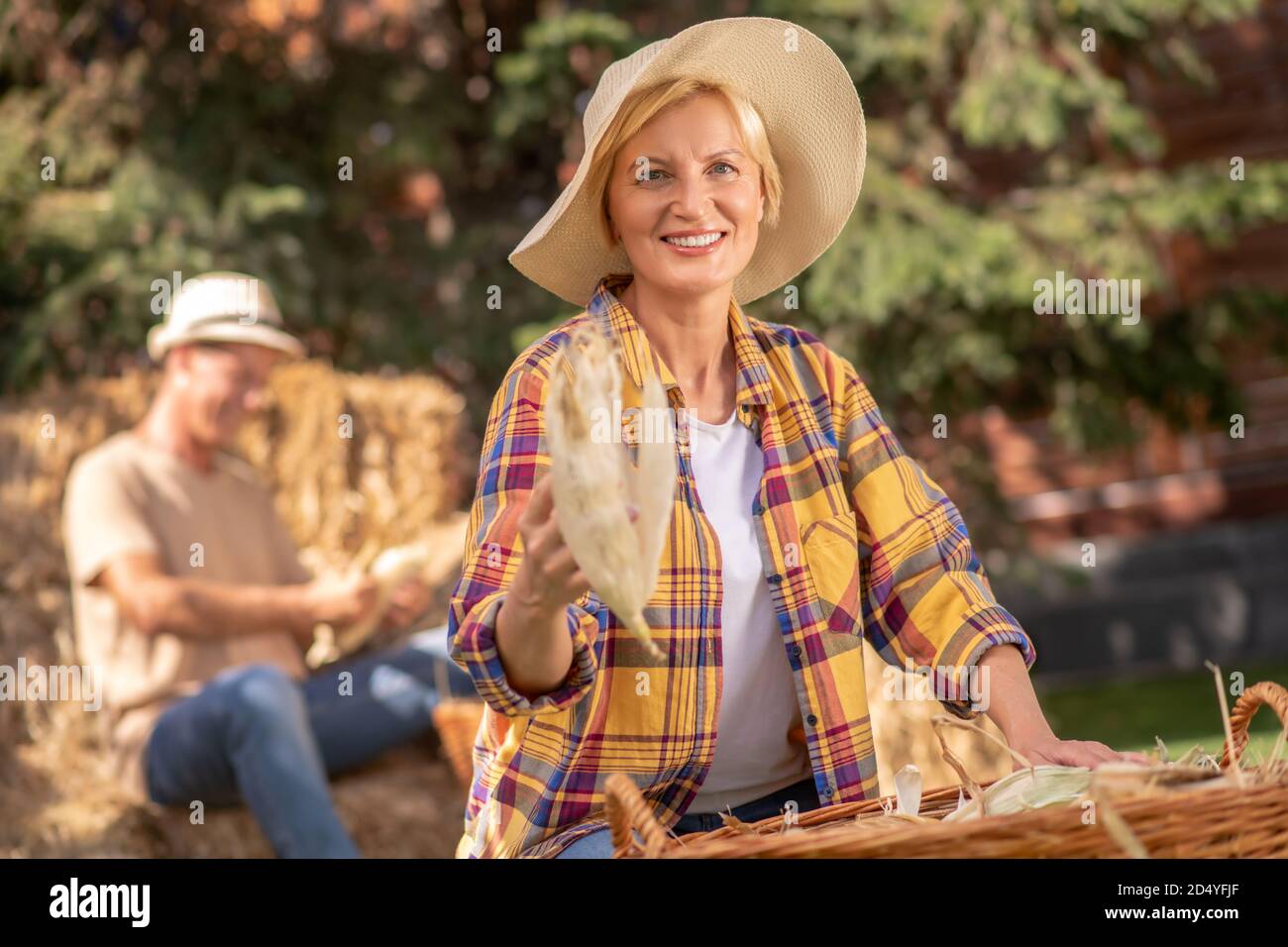 Bäuerin im Strohhut zeigt Maiskolben in die Kamera Stockfoto