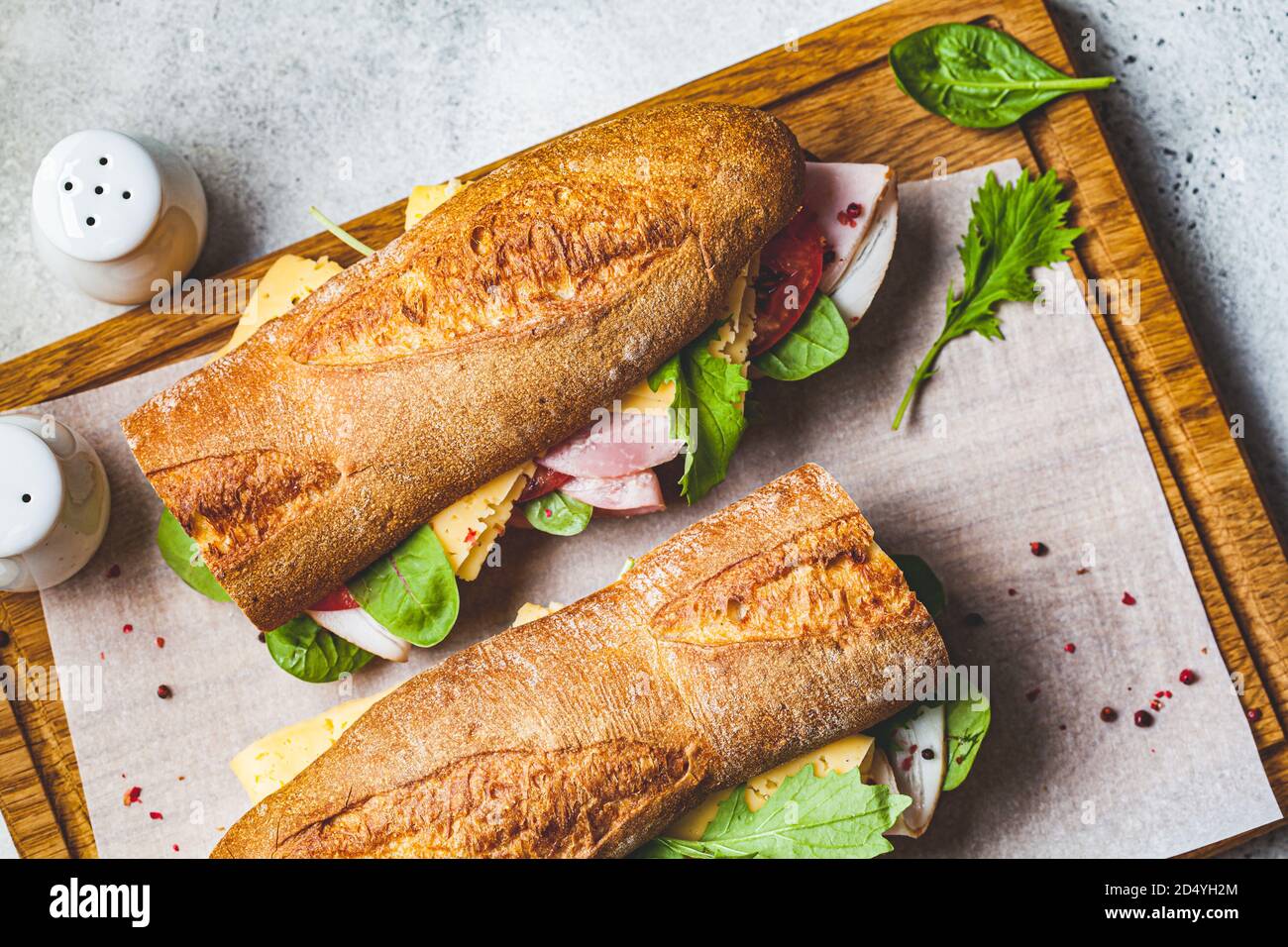 Baguette-Sandwich mit Fleisch, Käse und Gemüse auf einem Holzbrett. Stockfoto