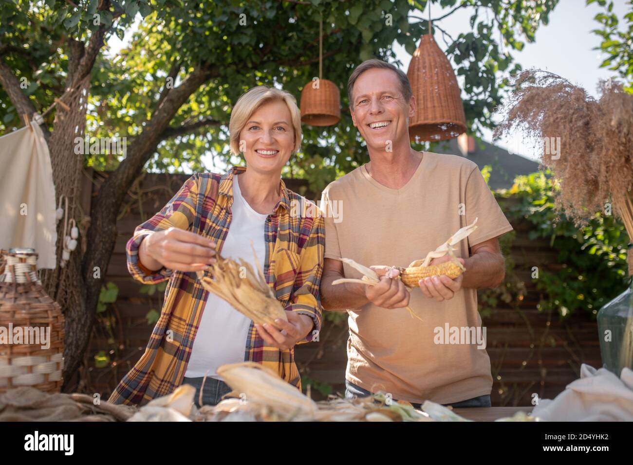 Glückliches Paar mittleren Alters, das im Garten Mais schüttelt und lächelt Stockfoto