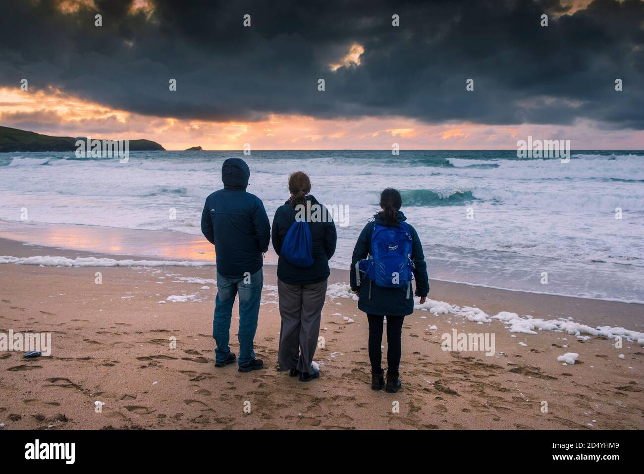 Eine Familie von Urlaubern, die am Fistral Beach stehen und einen spektakulären Sonnenuntergang in Newquay in Cornwall beobachten. Stockfoto