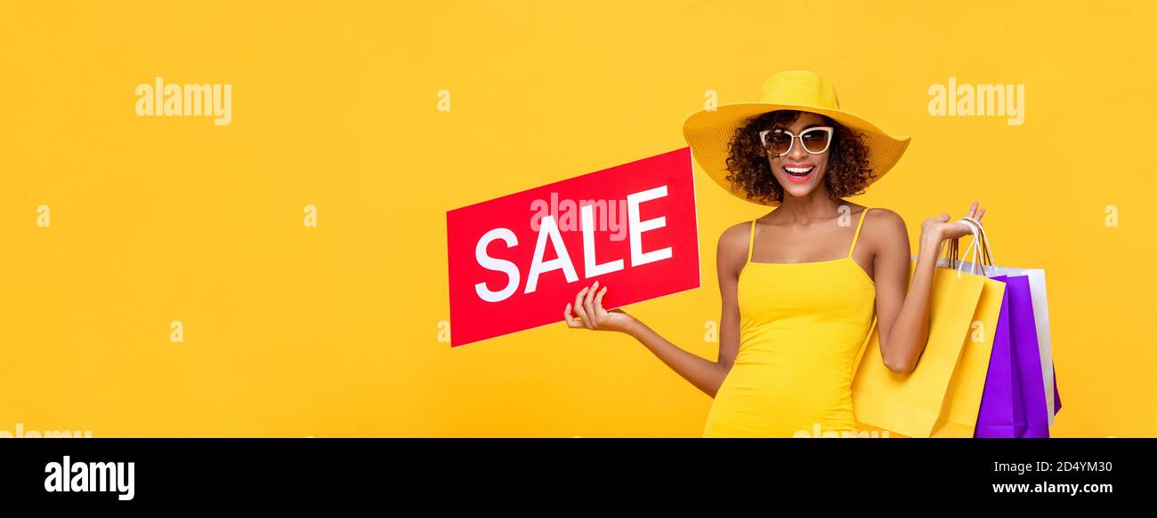 Überrascht modische afroamerikanische Frau trägt Einkaufstaschen und rot Verkaufsschild in isoliertem gelben Banner-Hintergrund mit Kopierplatz Stockfoto