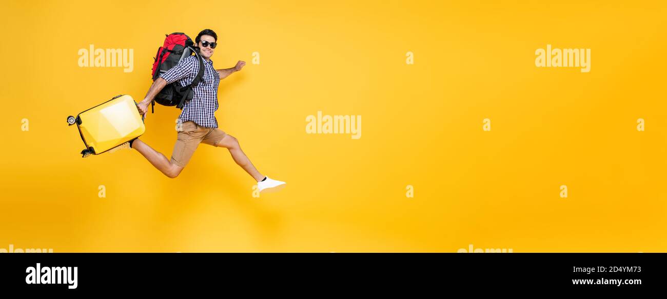 Junge aufgeregt kaukasischen männlichen Touristen mit Gepäck springen in der Luft Isoliert auf bunten Studio gelben Banner Hintergrund mit Kopierraum Stockfoto Junge aufgeregt kaukasischen männlichen Touristen mit Gepäck springen in der Luft Isoliert auf bunten Studio gelben Banner Hintergrund mit Kopierraum Stockfoto