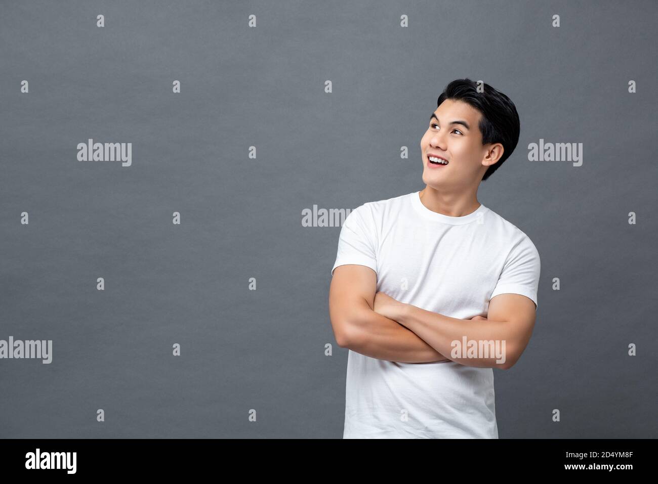 Taille bis Porträt von gut aussehend fröhlich asiatischen Mann in Armen Gekreuzte Geste Blick auf leeren Raum neben isolierten grauen Hintergrund Stockfoto