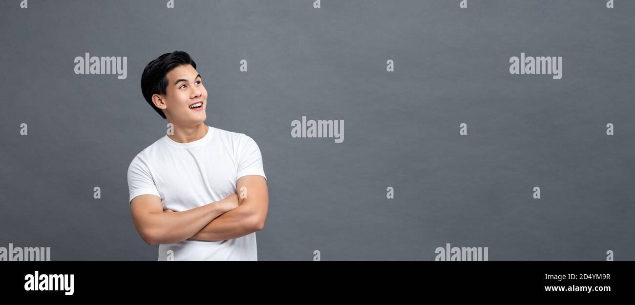 Taille bis Porträt von gut aussehend fröhlich asiatischen Mann in Armen Gekreuzte Geste Blick auf leeren Raum neben isolierten grauen Banner Hintergrund Stockfoto