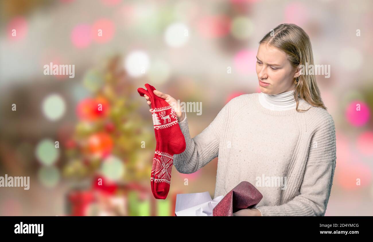 Ein enttäuschendes Weihnachtsgeschenk für eine junge Frau davor Von verschwommenem weihnachtshintergrund Stockfoto