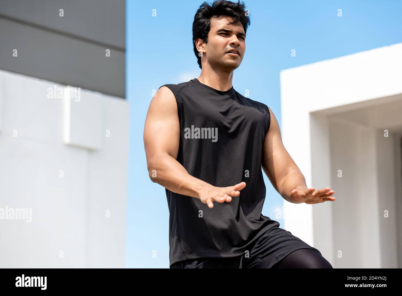 Schöner indischer Mann tun hohe Knie Tap Übung im Freien auf Gebäude Dach, Open Air Home Workout Konzept Stockfoto