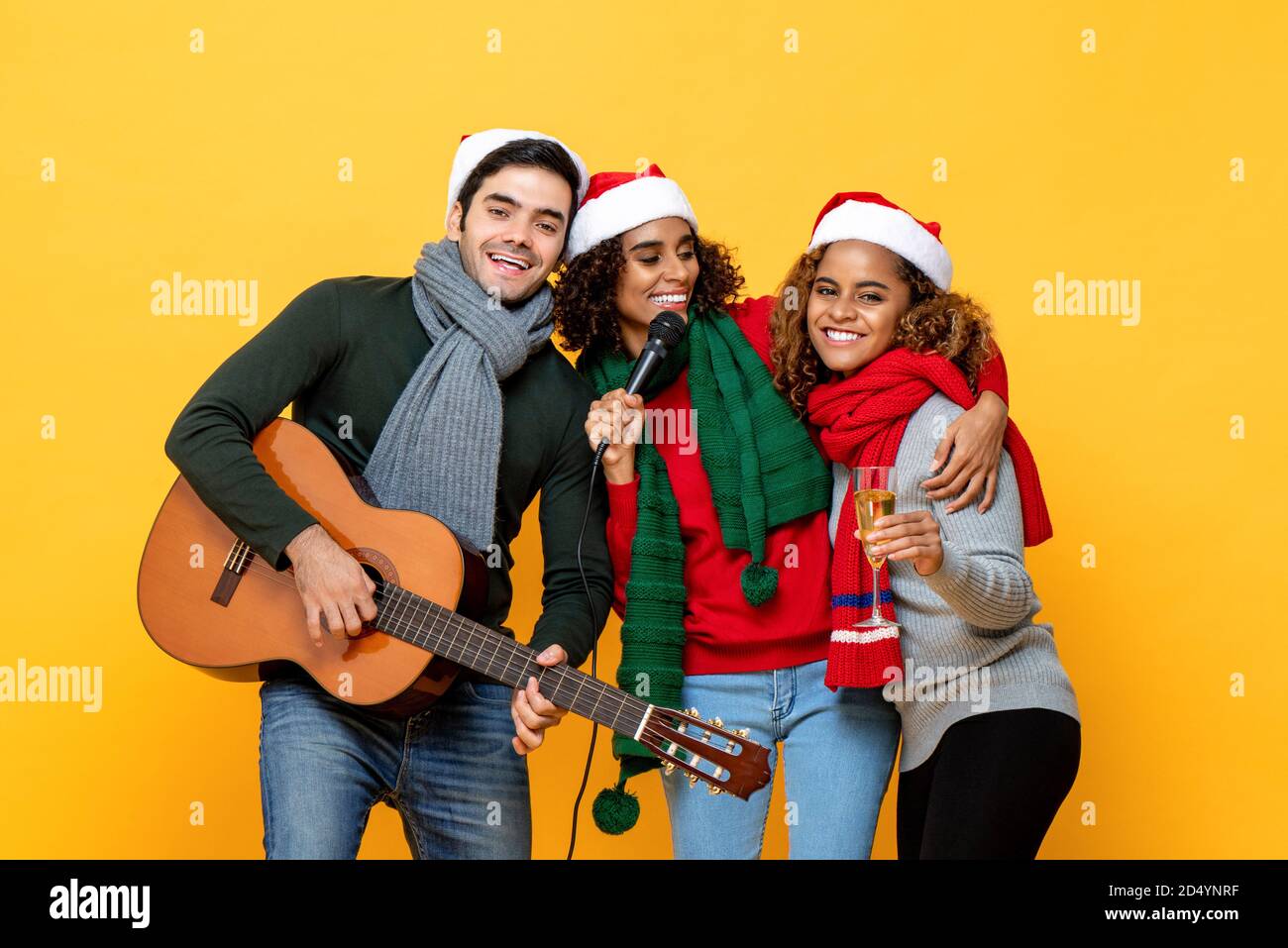 Glückliche drei verschiedene Freunde, die Party singen und Weihnachten feiern Im gelben Studio-Hintergrund Stockfoto