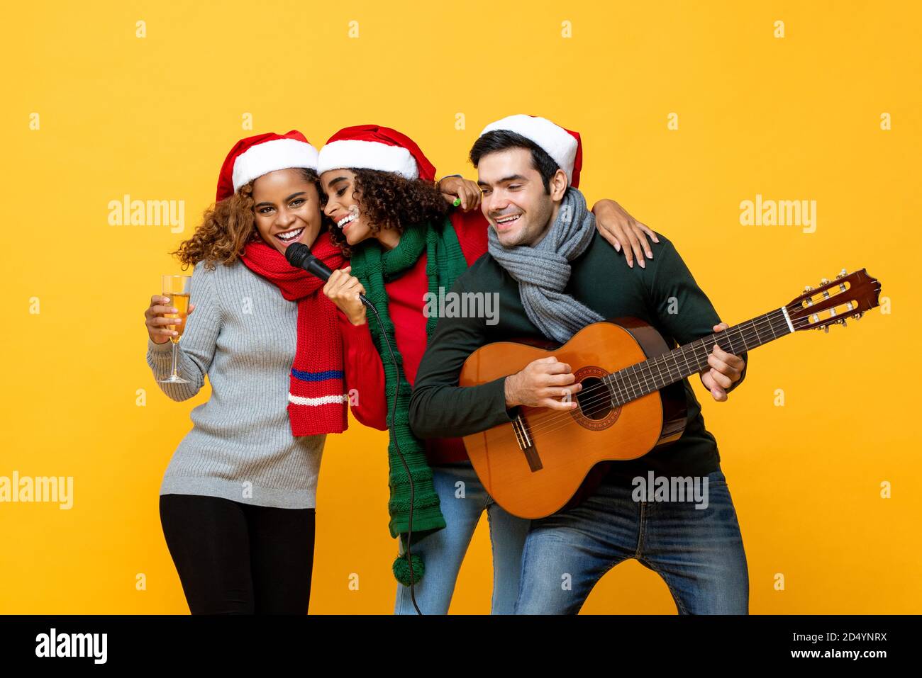 Glückliche drei verschiedene Freunde, die Party singen und Weihnachten feiern Im gelben Studio-Hintergrund Stockfoto