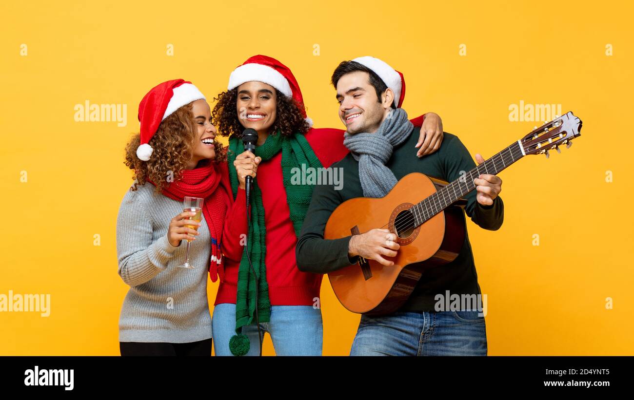 Fröhliche, vielfältige Freunde, die Party singen und Weihnachten feiern Gelber Studiohintergrund Stockfoto