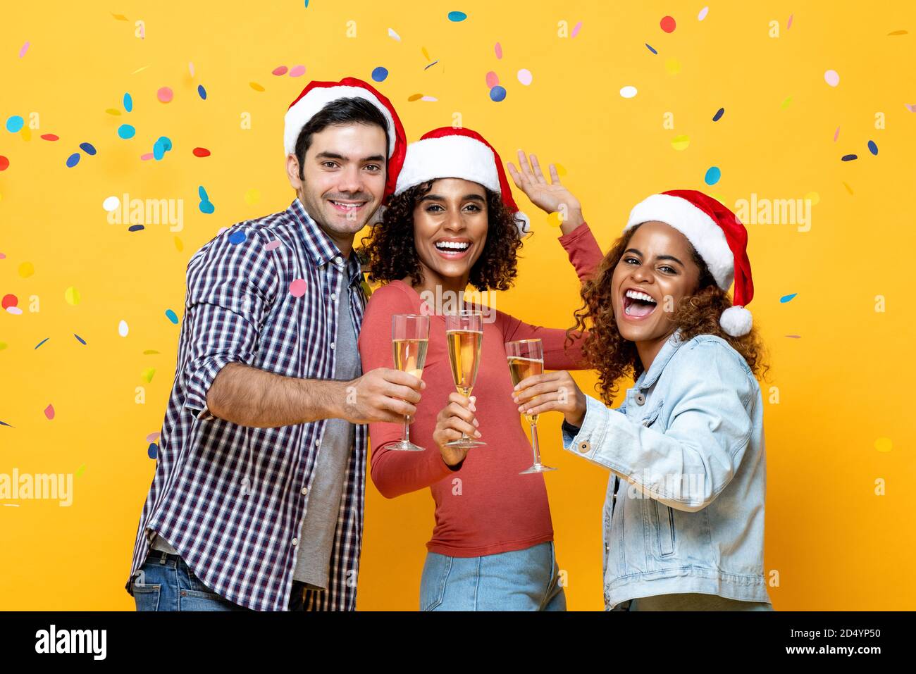 Eine Gruppe von glücklichen, vielfältigen Freunden feiert Weihnachten und trinkt gemeinsam Champagner Auf gelbem Studiohintergrund mit Konfetti Stockfoto