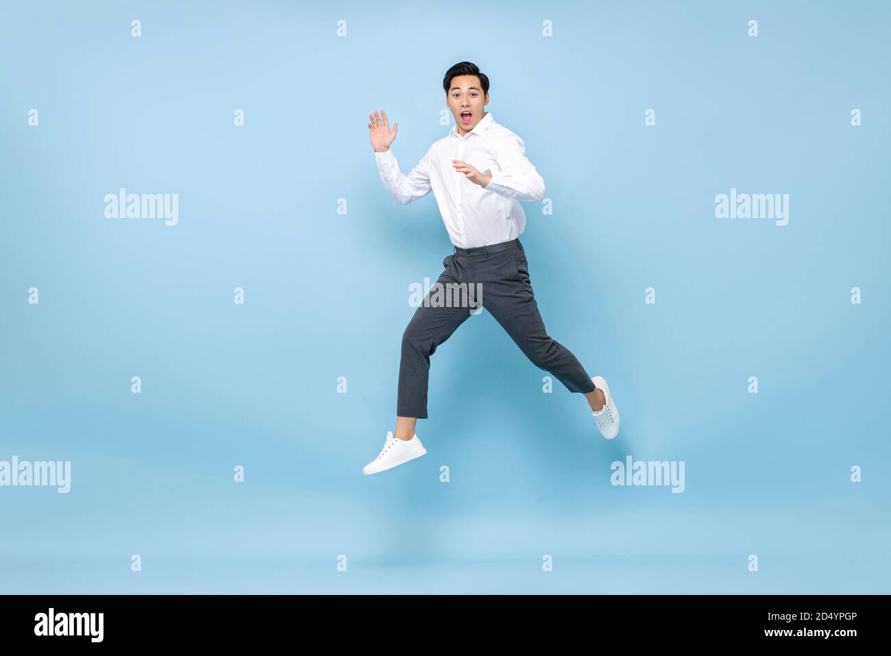 Energetische asiatische Mann in semi formale Kleidung springen in der Mitte Luft auf hellblauem Hintergrund isoliert Stockfoto