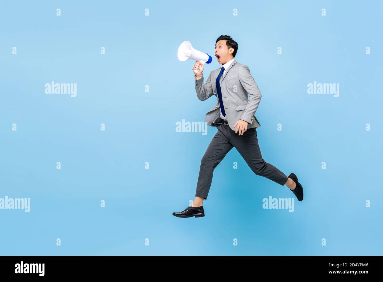 Überrascht junge asiatische Geschäftsmann springen und schreien auf Megaphon isoliert Auf hellblauem Hintergrund mit Kopierplatz Stockfoto