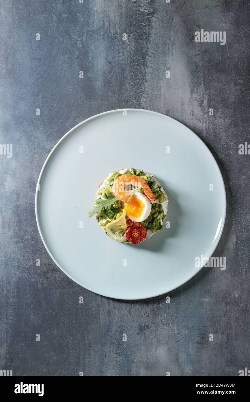 Vegetarisches Sandwich mit gehackten Avocado, sonnengetrocknete Tomaten, Ei, Krabben, Frischkäse serviert auf keramische Platte über blaue Textur Hintergrund. Wohnung La Stockfoto