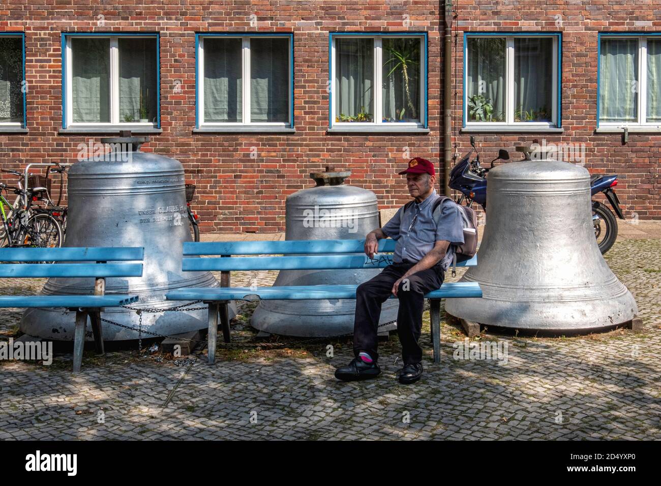 Älterer Mann sitzt neben alten Stahlglocken vor der Matthäus-Kirche, Matthäus-Kirche, in Steglitz, Berlin Stockfoto