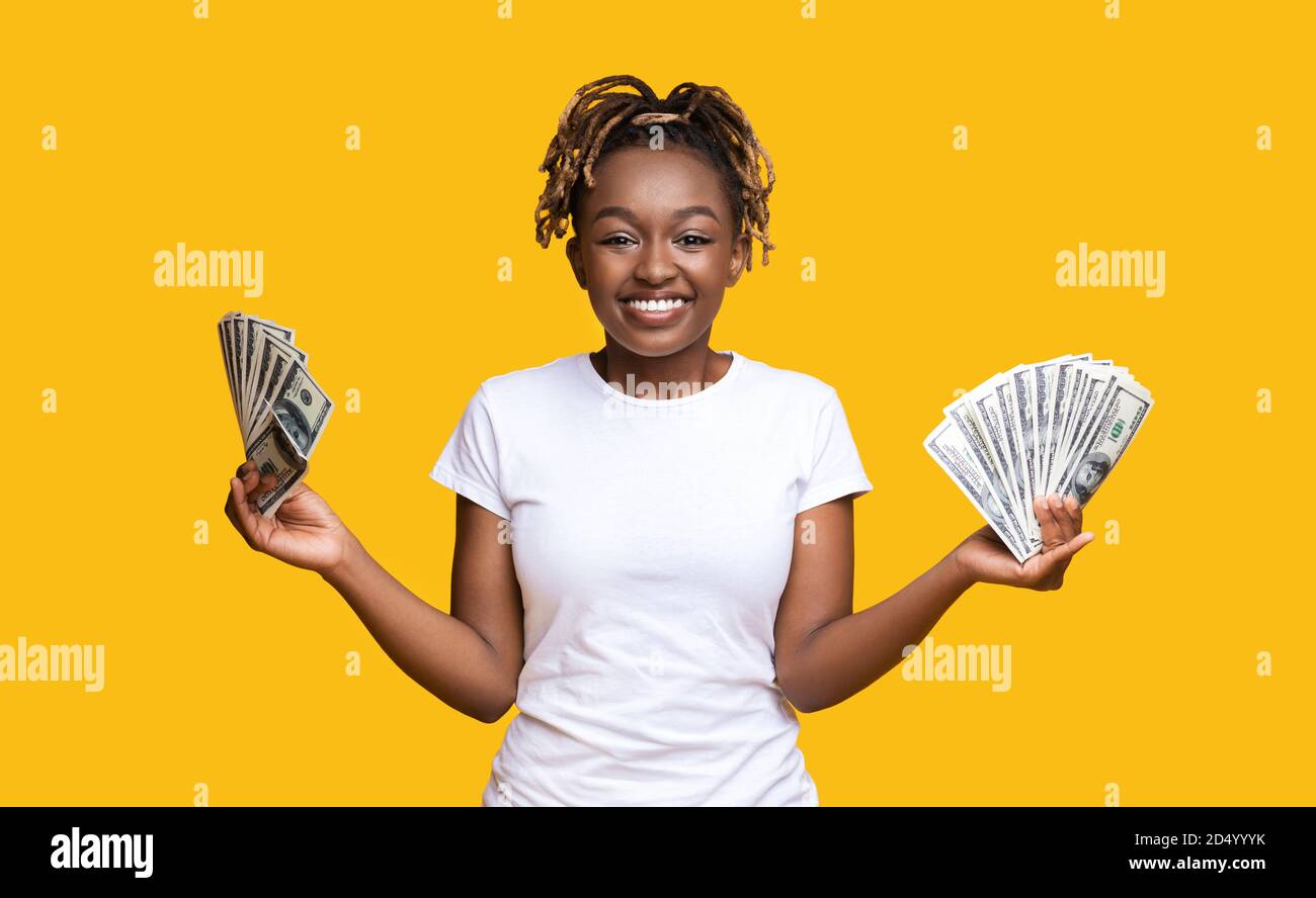 Emotionale afroamerikanische Frau, die Geld in beiden Händen hält Stockfoto